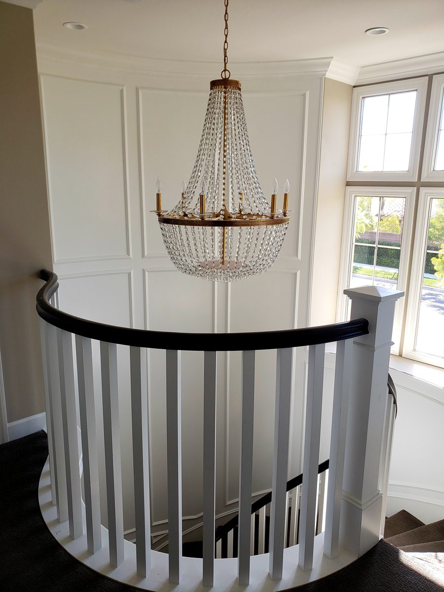 Curved upper-floor railing overlooking the stairwell, with a crystal chandelier and paneled wall